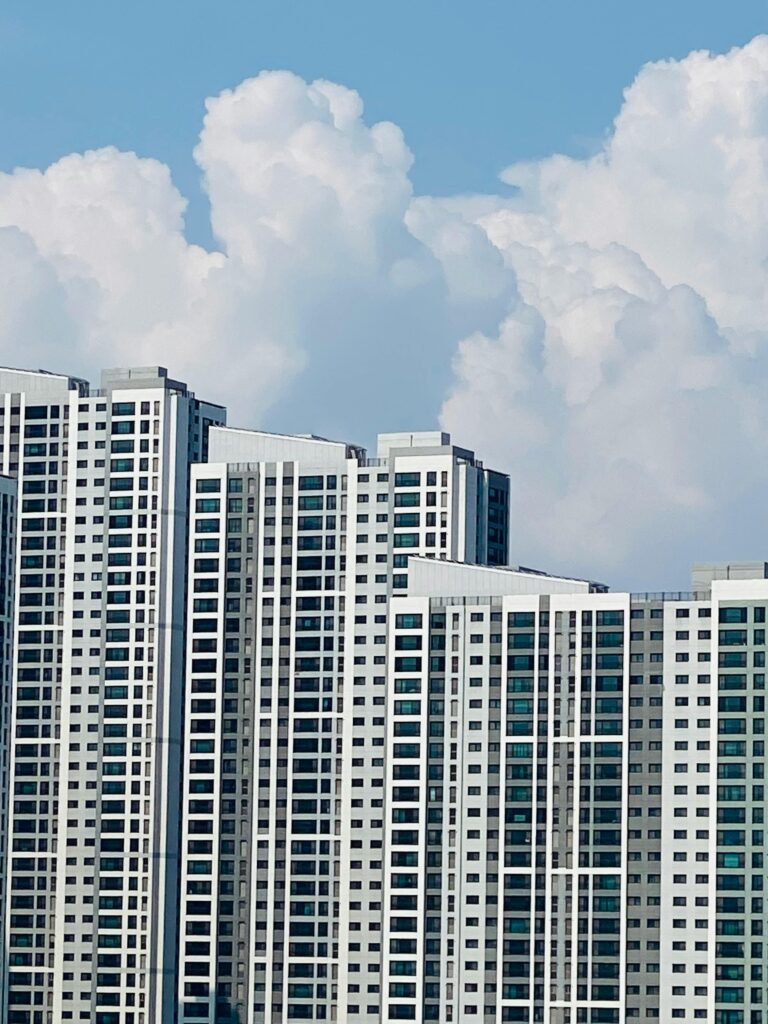 High-rise apartment buildings in Seoul under a clear blue sky with dramatic white clouds.