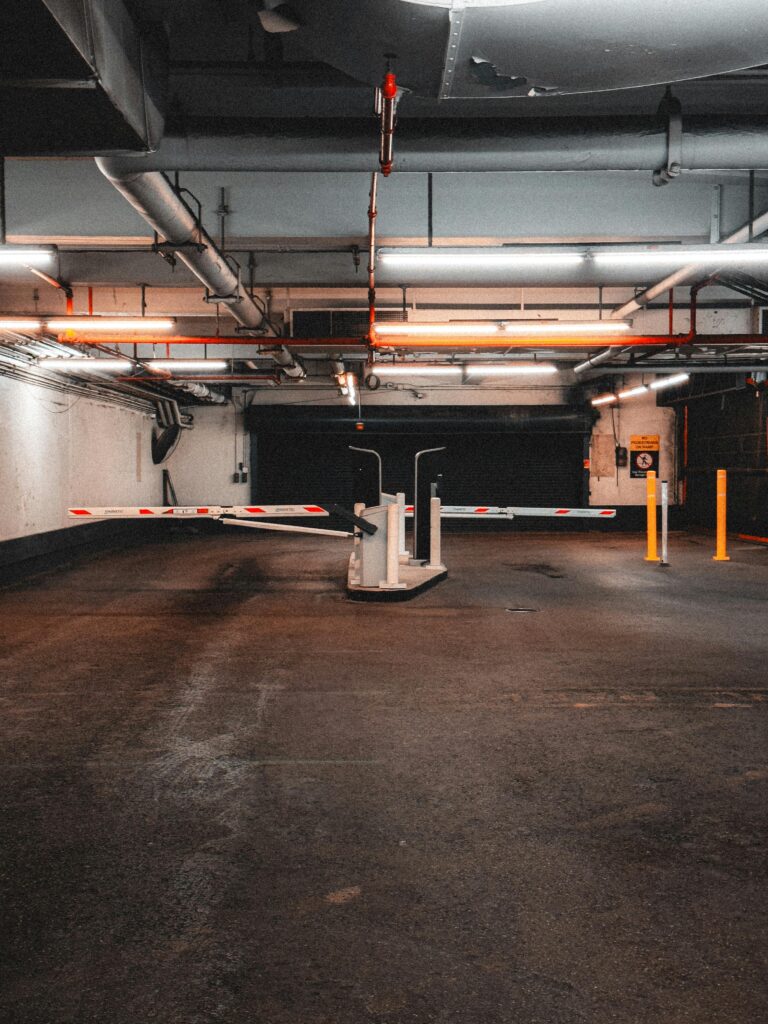 Explore the industrial ambiance of a dimly lit parking garage with visible barriers and pipes.